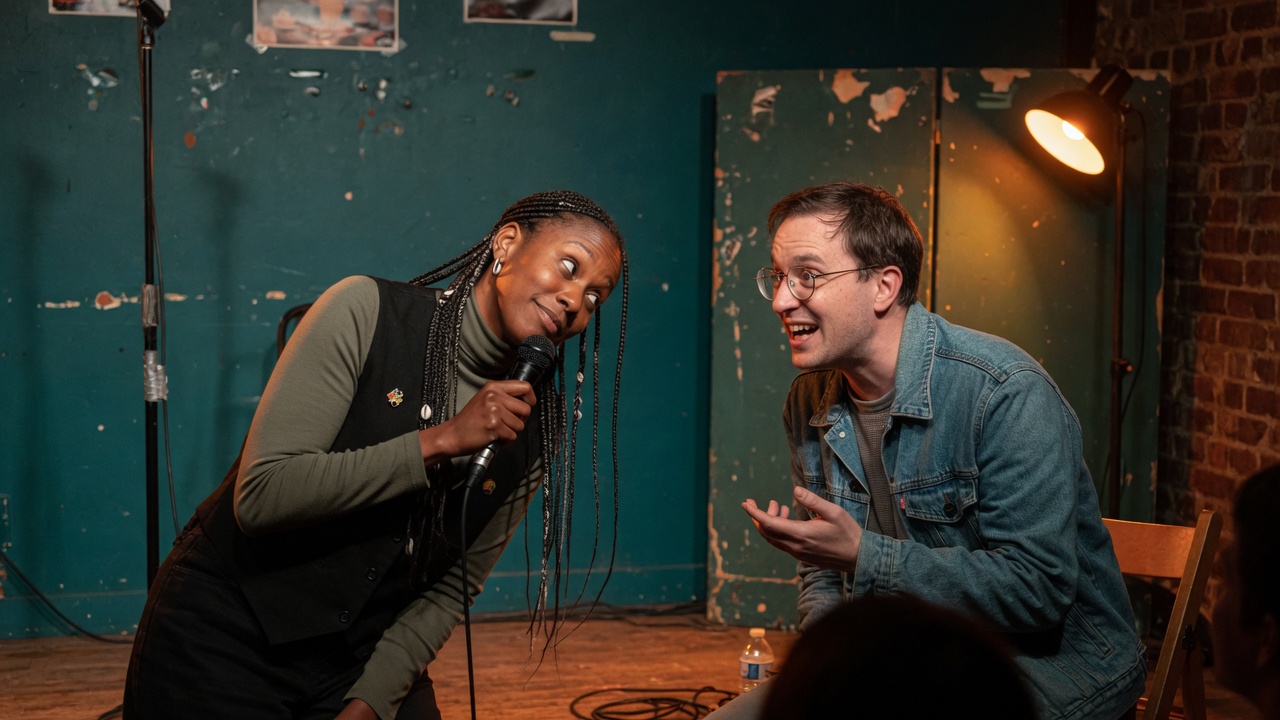 Two fictional adults share a handheld microphone in a small teal room
